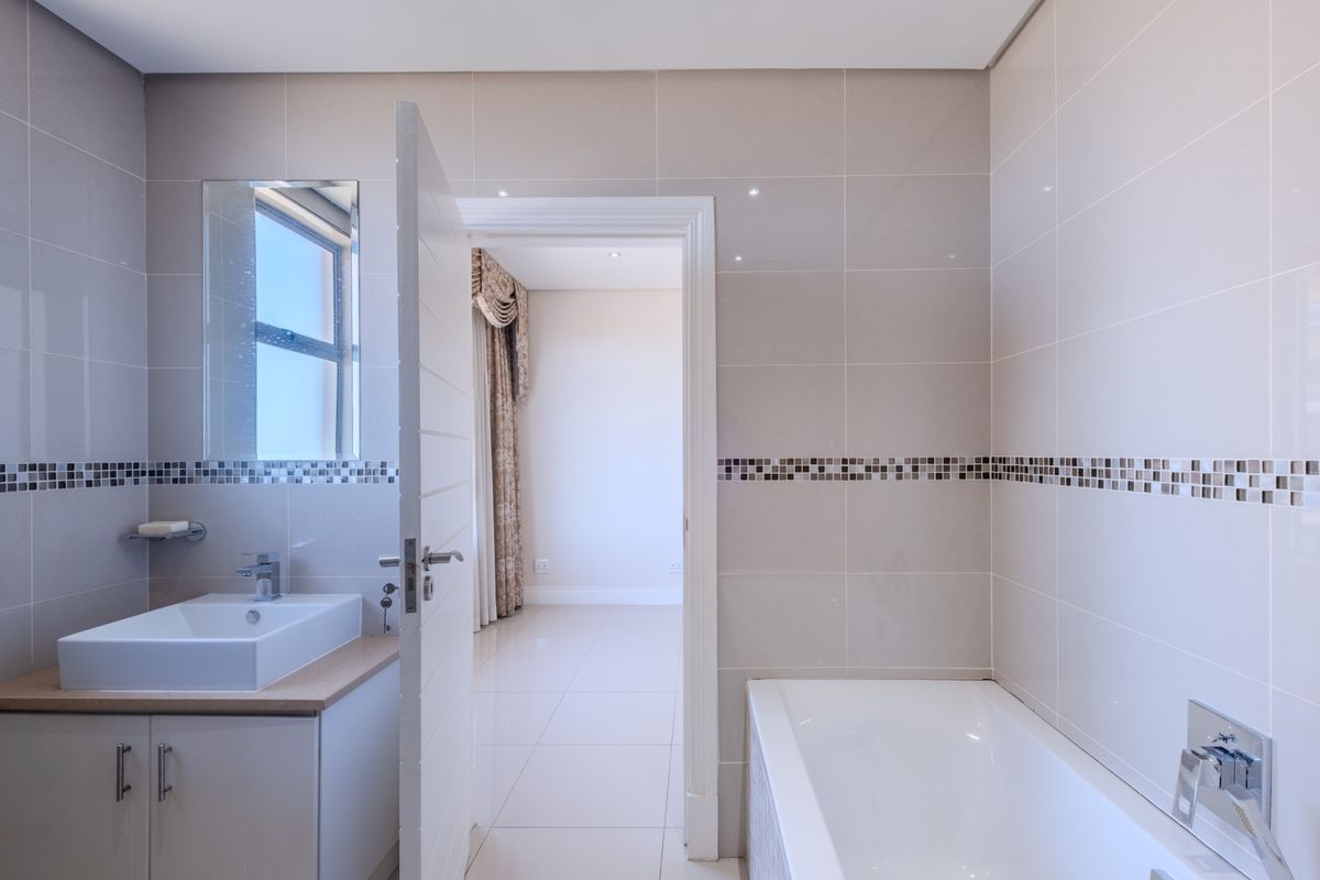 Modern bathroom featuring a vanity with basin, bathtub, neutral wall tiling with mosaic accents, and recessed lighting, with an adjacent room visible.