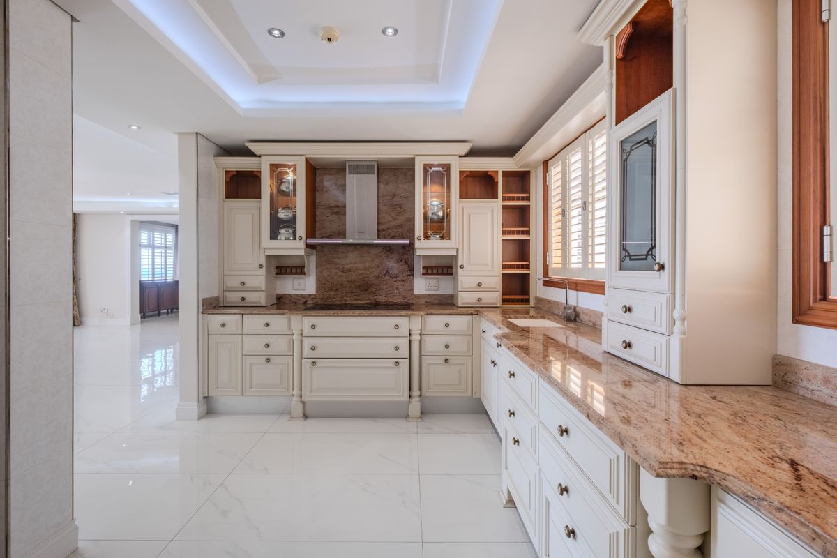 A spacious, high-end kitchen featuring custom cabinetry, granite countertops, integrated extractor fan, and elegant marble-look flooring with sophisticated recessed and cove lighting.