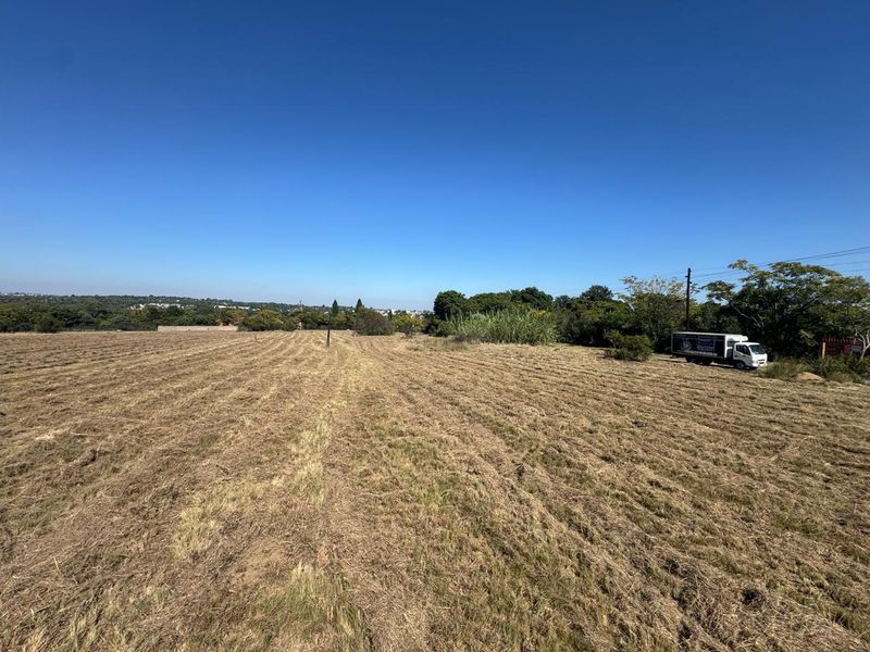 A wide-angle view of a large, cleared residential vacant land plot with mature trees in the background.
