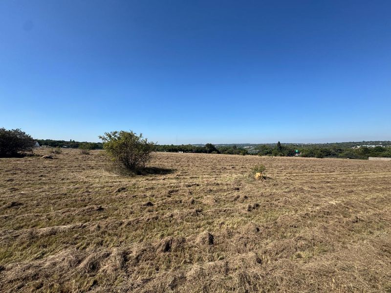 A wide-angle view of a vacant residential plot featuring cleared grass and distant landscape views under a clear blue sky.