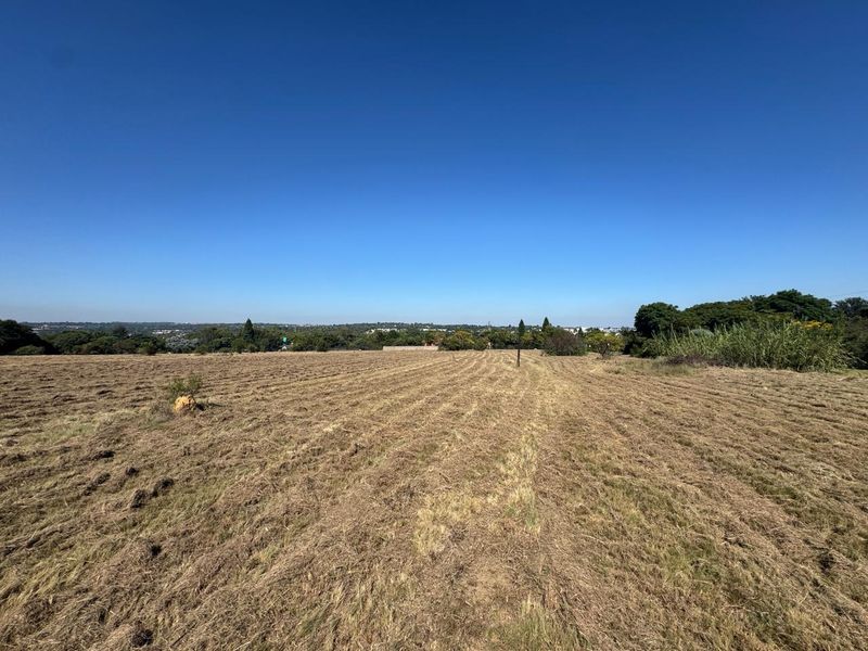 A wide-angle view of a large, cleared vacant residential plot with natural landscape and distant horizon.