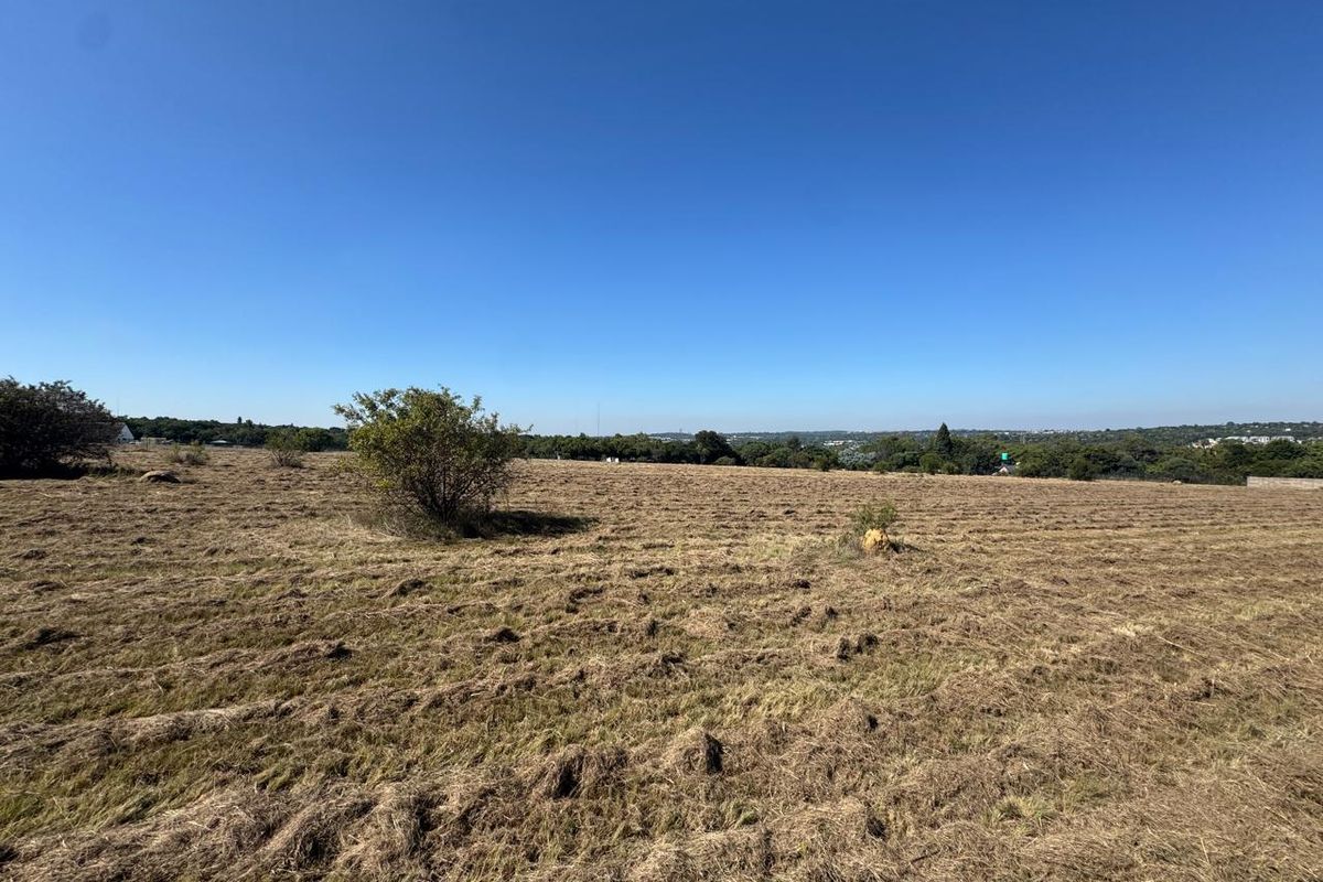 A wide-angle view of a vacant residential plot featuring cleared grass and distant landscape views under a clear blue sky.