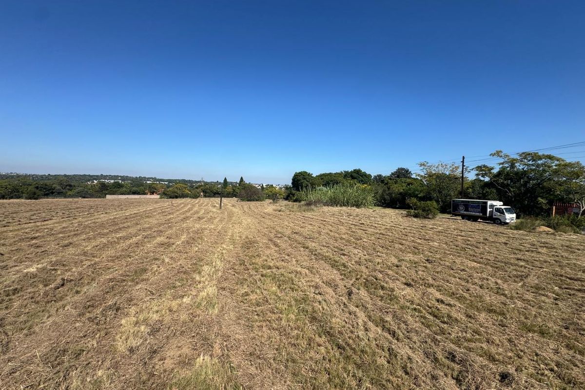 A wide-angle view of a large, cleared residential vacant land plot with mature trees in the background.