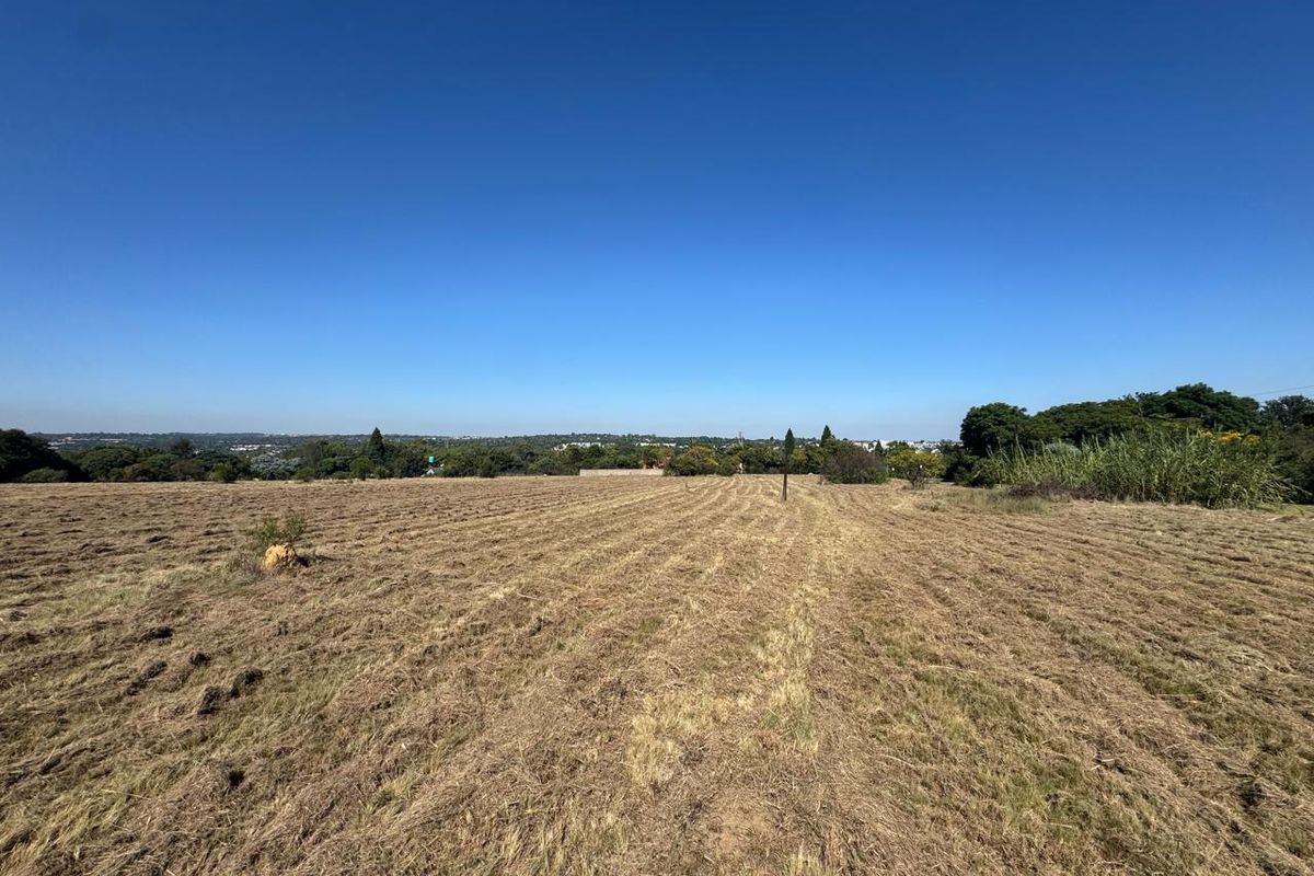 A wide-angle view of a large, cleared vacant residential plot with natural landscape and distant horizon.