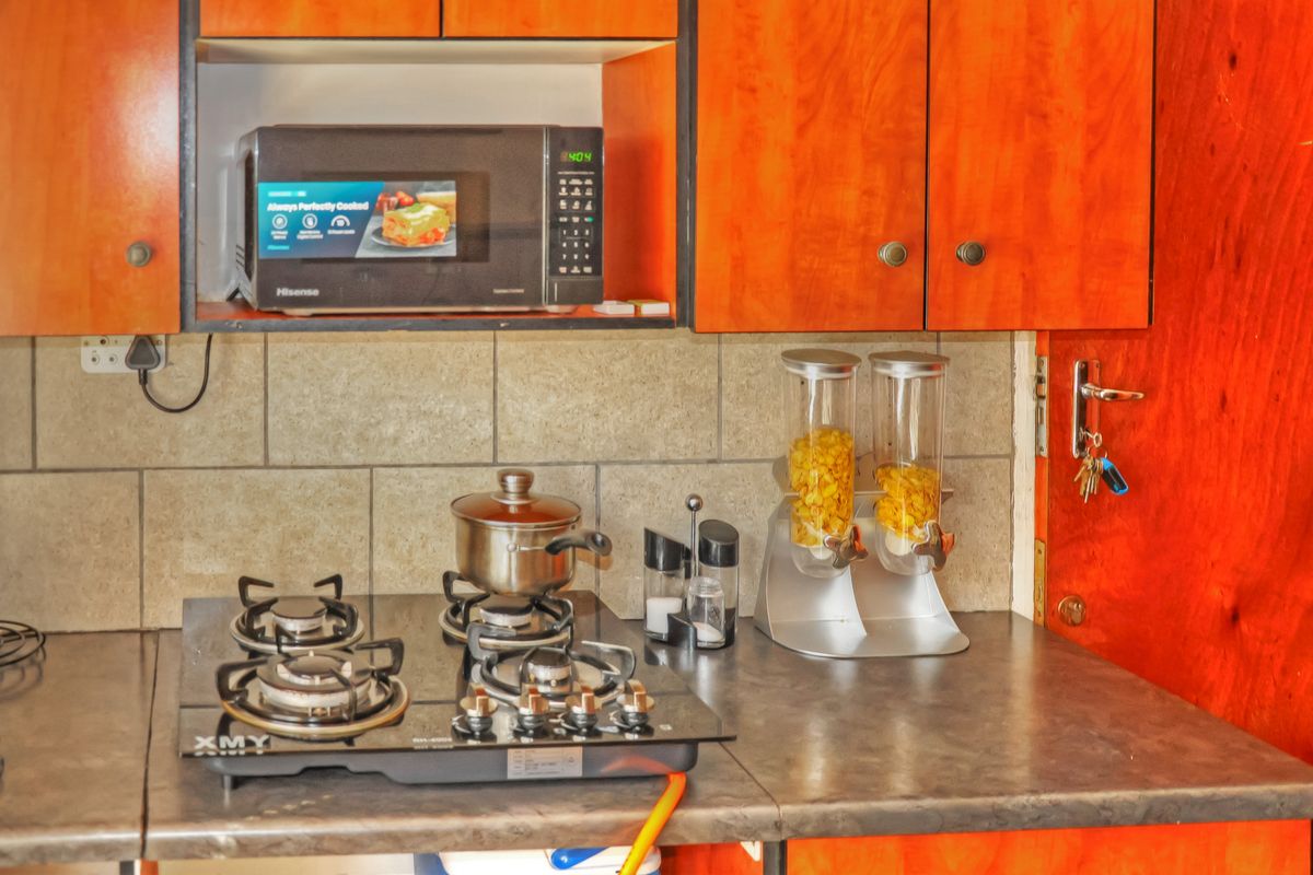 A kitchen workspace featuring wood-veneer cabinetry, a stone-look laminate countertop, a built-in microwave niche, and a gas hob with a tiled backsplash.