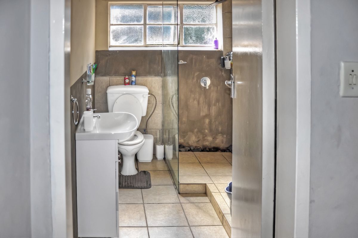 A compact bathroom featuring a walk-in shower with glass partition, pedestal basin, and toilet, finished with neutral floor tiles.
