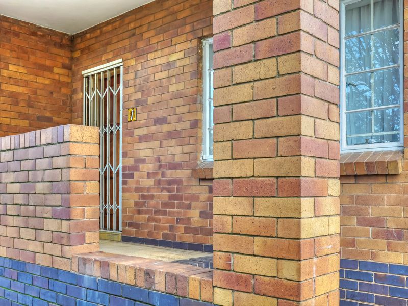 A covered front entrance featuring classic face-brick construction, a security gate, and a brick pillar, providing a secure and traditional townhouse entry.