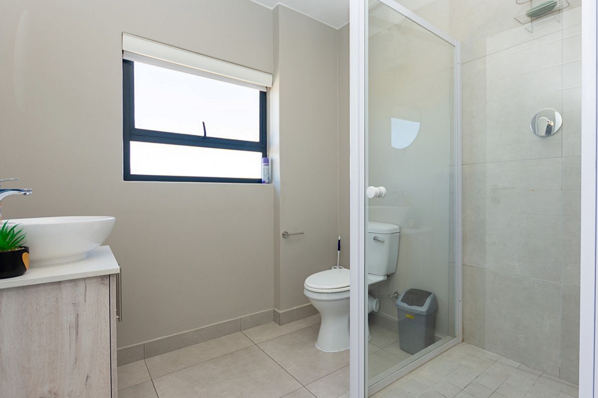 A modern bathroom featuring a glass-enclosed shower, a vessel sink vanity, and a standard toilet with neutral floor and wall tiling.