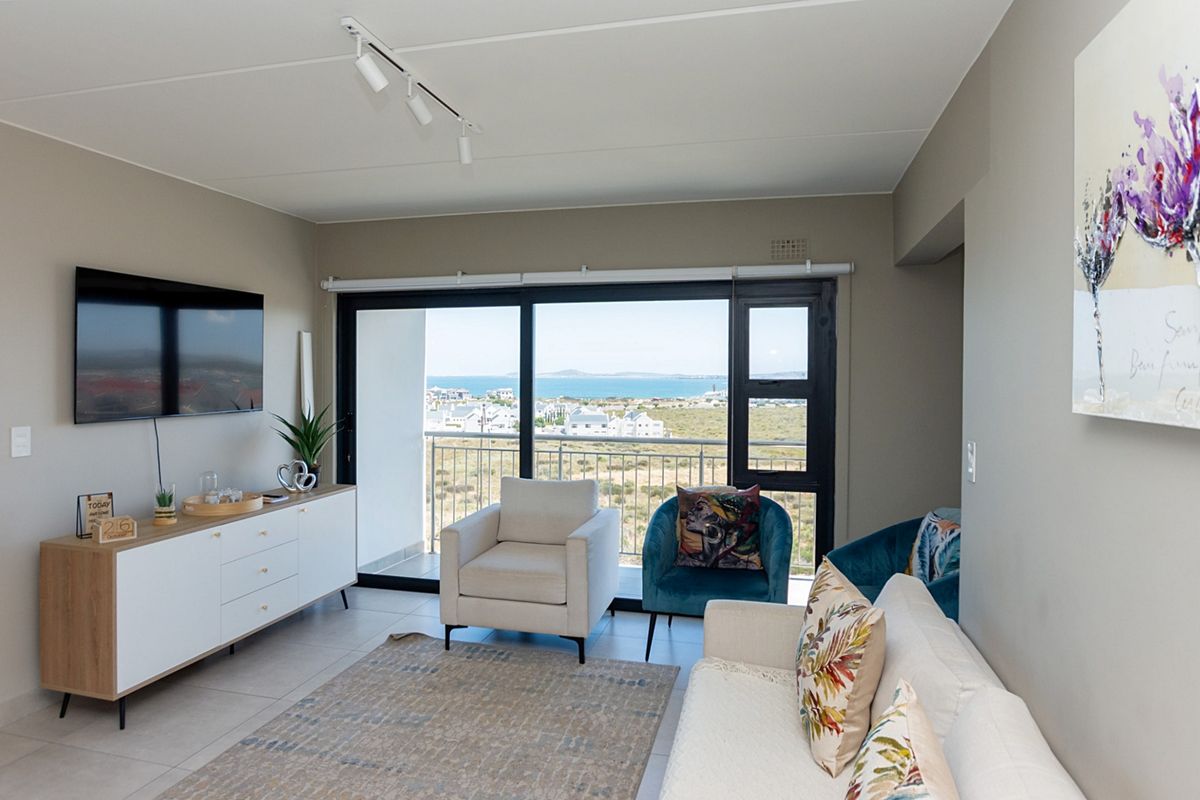 A bright living room featuring large sliding glass doors that open to a balcony with scenic coastal and ocean views.