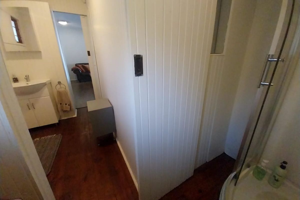 A functional bathroom featuring a vanity unit, shower enclosure, and timber-look flooring, with a view leading into an adjacent living space.