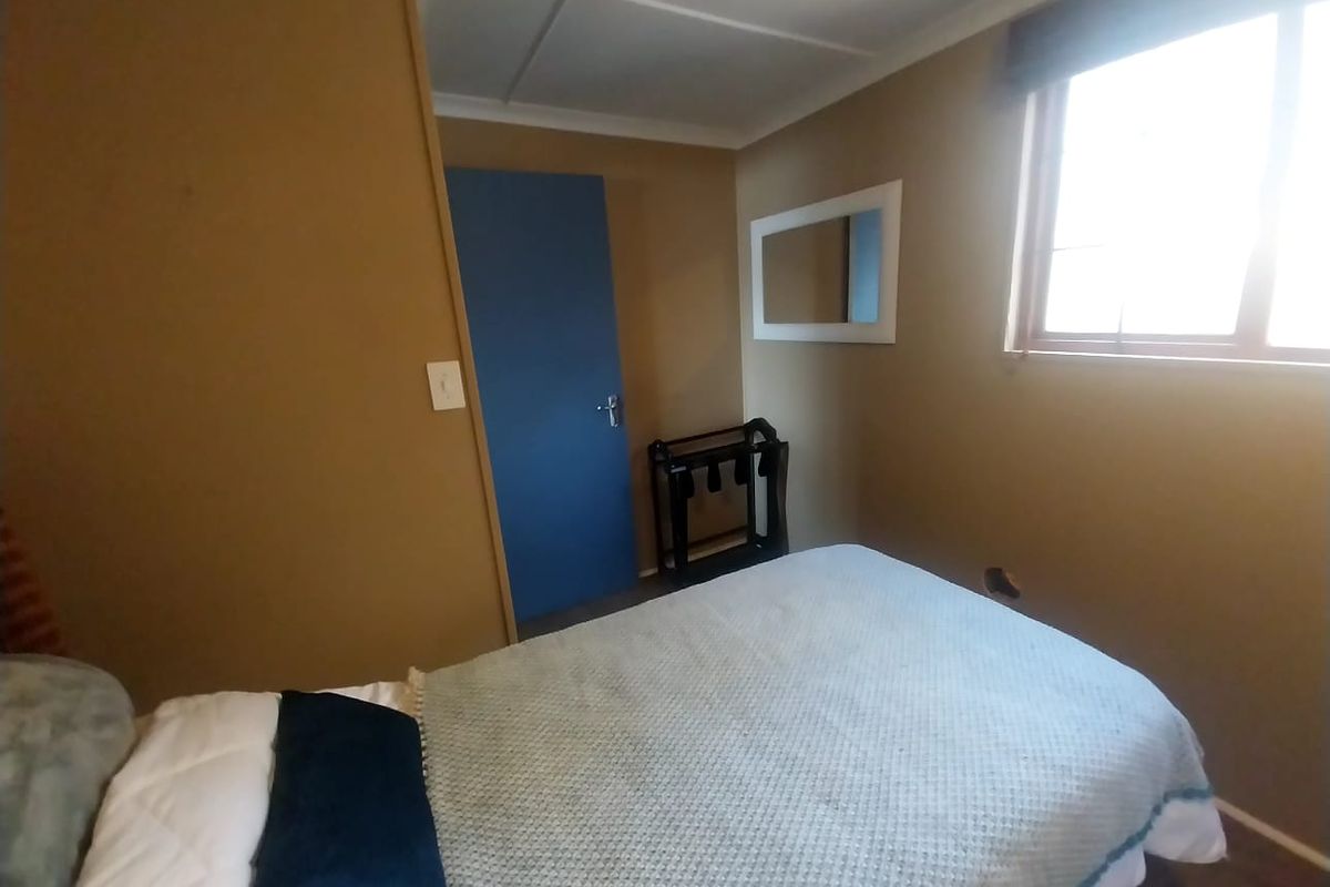 A bedroom featuring neutral-toned walls, a window with natural light, and a blue interior door.