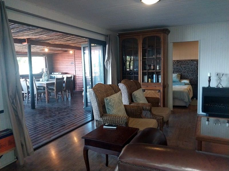 Open plan living area featuring timber flooring, wood-paneled walls, and seamless transition to a covered outdoor patio through large sliding glass doors.