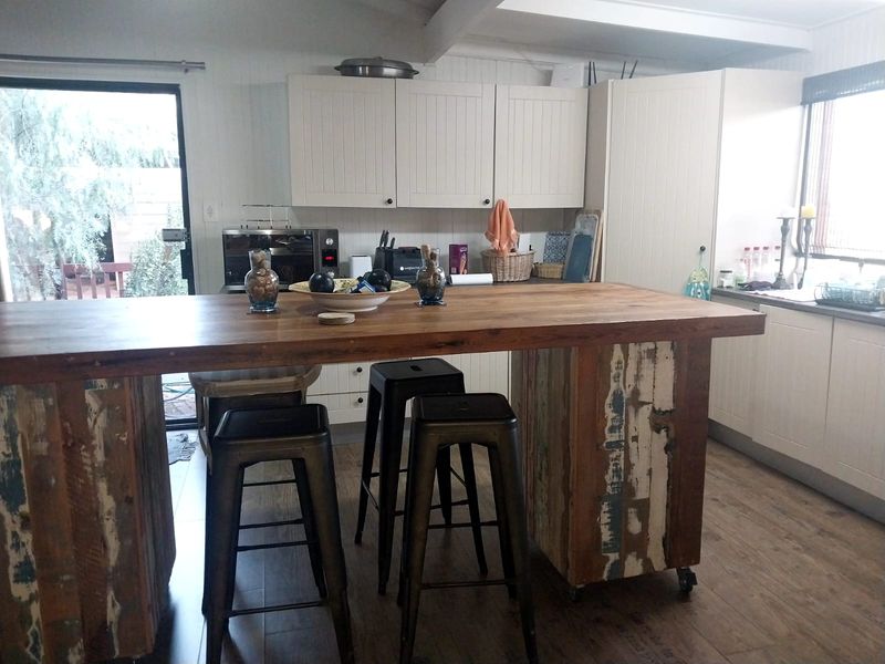 A rustic kitchen featuring a large wooden island with a distressed finish, white cabinetry, and wood-look flooring with direct access to the outdoor area.