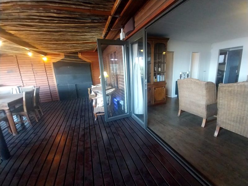Spacious covered patio featuring timber decking and a built-in braai, seamlessly connecting to the interior living area through large glass doors.