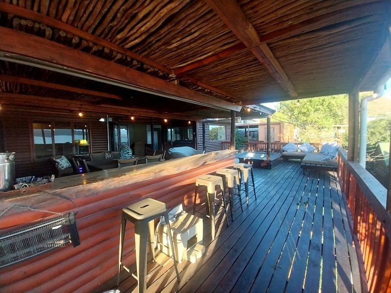Spacious covered outdoor patio featuring a built-in timber bar, rustic pole ceiling, and expansive wooden decking, ideal for outdoor entertaining.