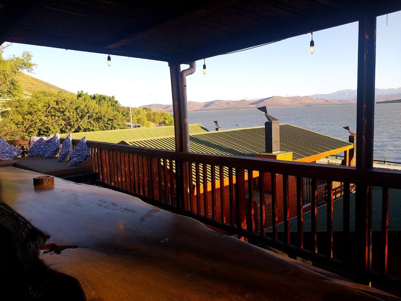 Covered wooden balcony featuring a built-in timber bar counter, offering expansive views of the lake and surrounding landscape.