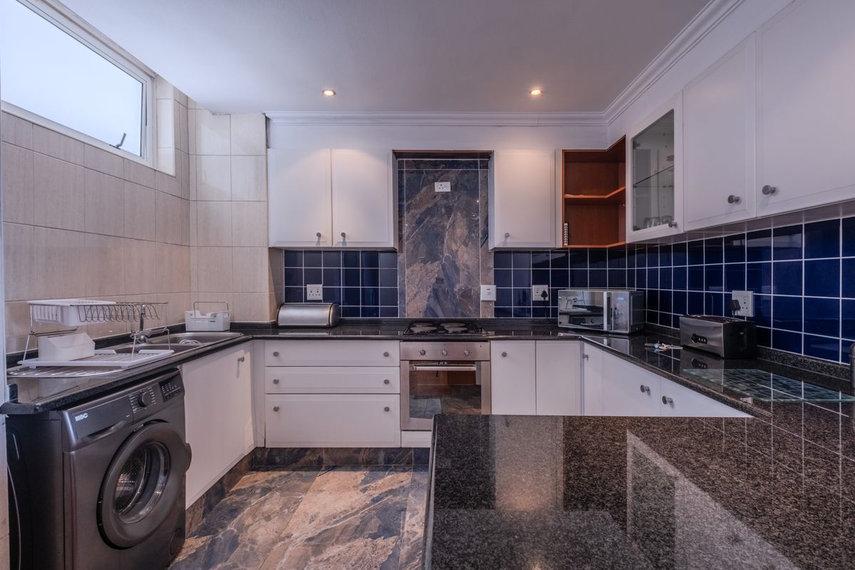 A well-appointed kitchen featuring granite countertops, built-in oven, gas hob, and ample cabinetry with a stylish tiled splashback and integrated laundry space.