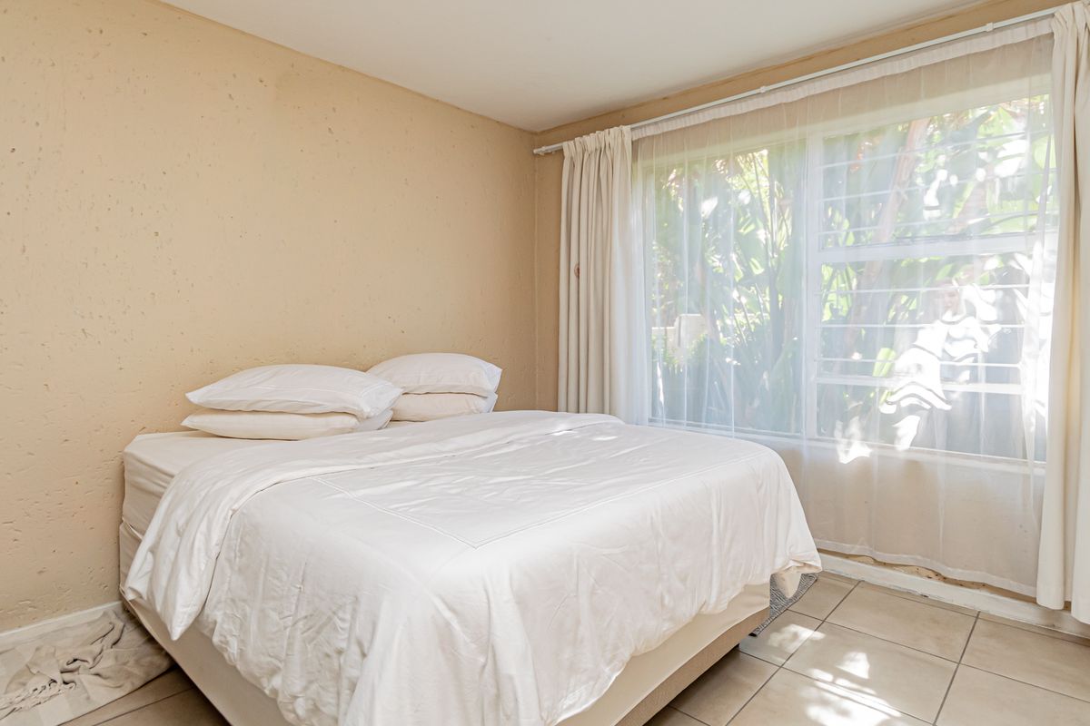 A bedroom featuring textured walls, tiled flooring, and a large window with security bars, providing natural light.