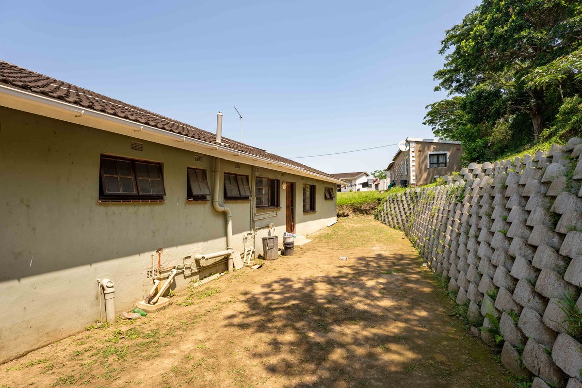 Rear exterior view of the property featuring a concrete block retaining wall, tiled roof, and exposed exterior plumbing along the side facade.