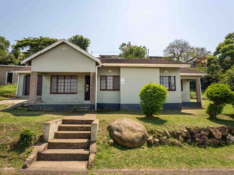 Front view of a single-story house featuring a tiled roof, brick pillars, and concrete entrance steps set within a landscaped garden.
