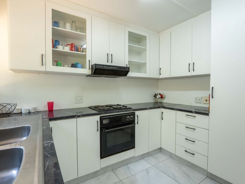 A functional kitchen featuring white cabinetry, dark marble-effect countertops, built-in oven, electric hob, extractor fan, and a double stainless steel sink.