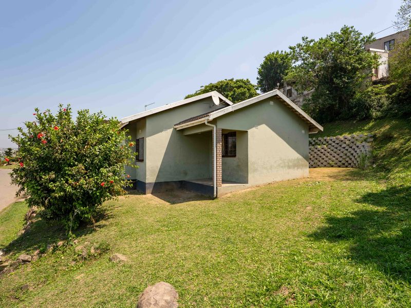 A view of the front exterior of a single-story house featuring a pitched roof, covered entrance porch, and a surrounding lawn with a retaining wall.
