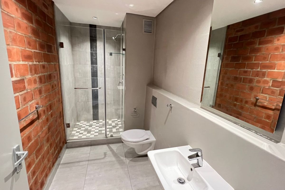 Modern bathroom featuring a glass-enclosed shower, wall-mounted toilet, vanity basin, and a striking exposed brick feature wall.