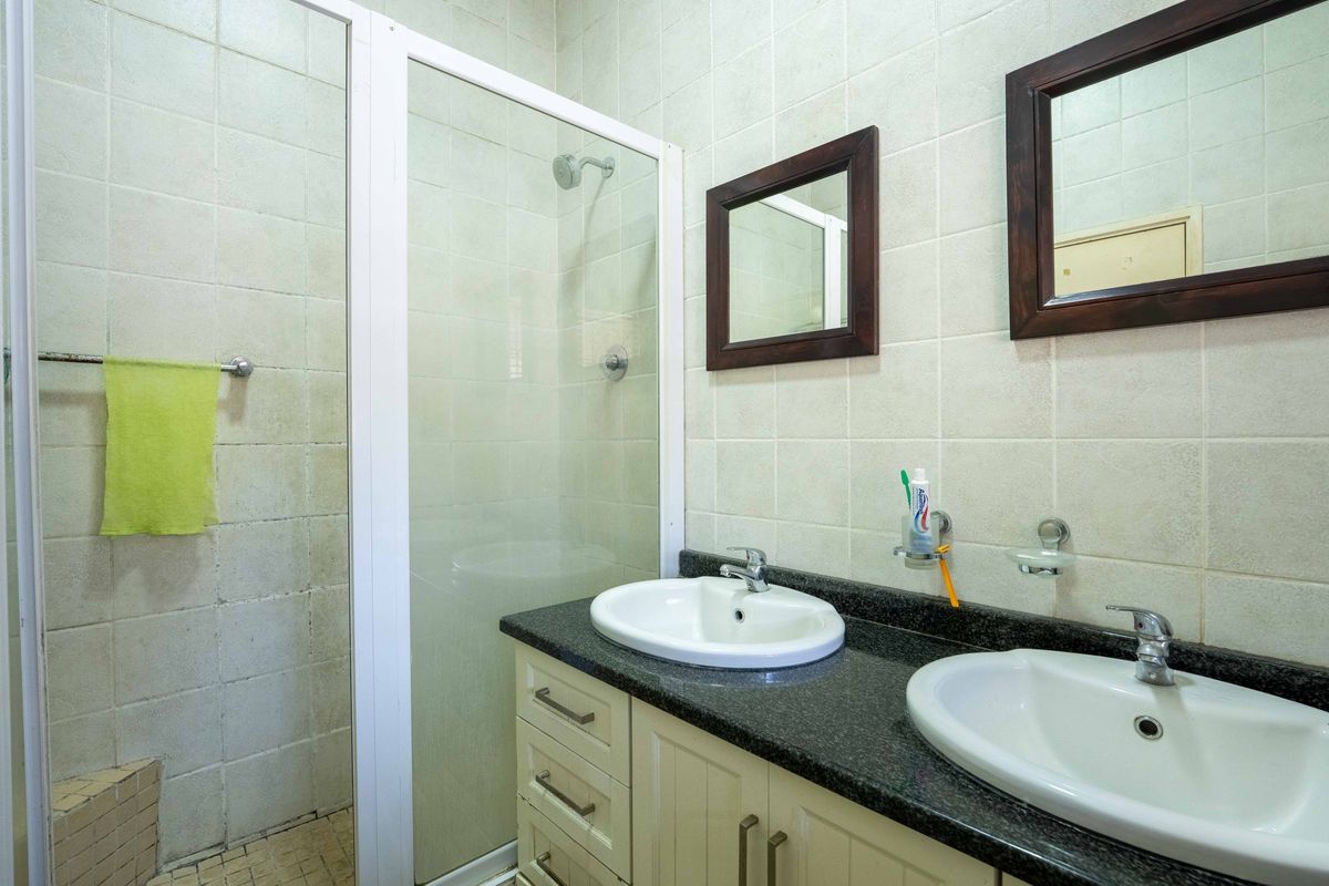 A functional bathroom featuring a double vanity with granite countertop, integrated sinks, and a glass-enclosed shower stall with tiled walls.