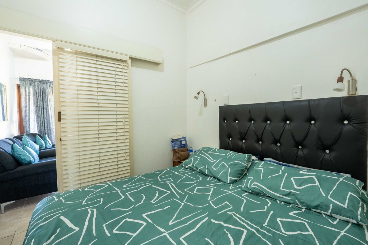 A bedroom featuring a sliding door partition, wall-mounted reading lights, and neutral finishes, with an adjacent view into a living area.