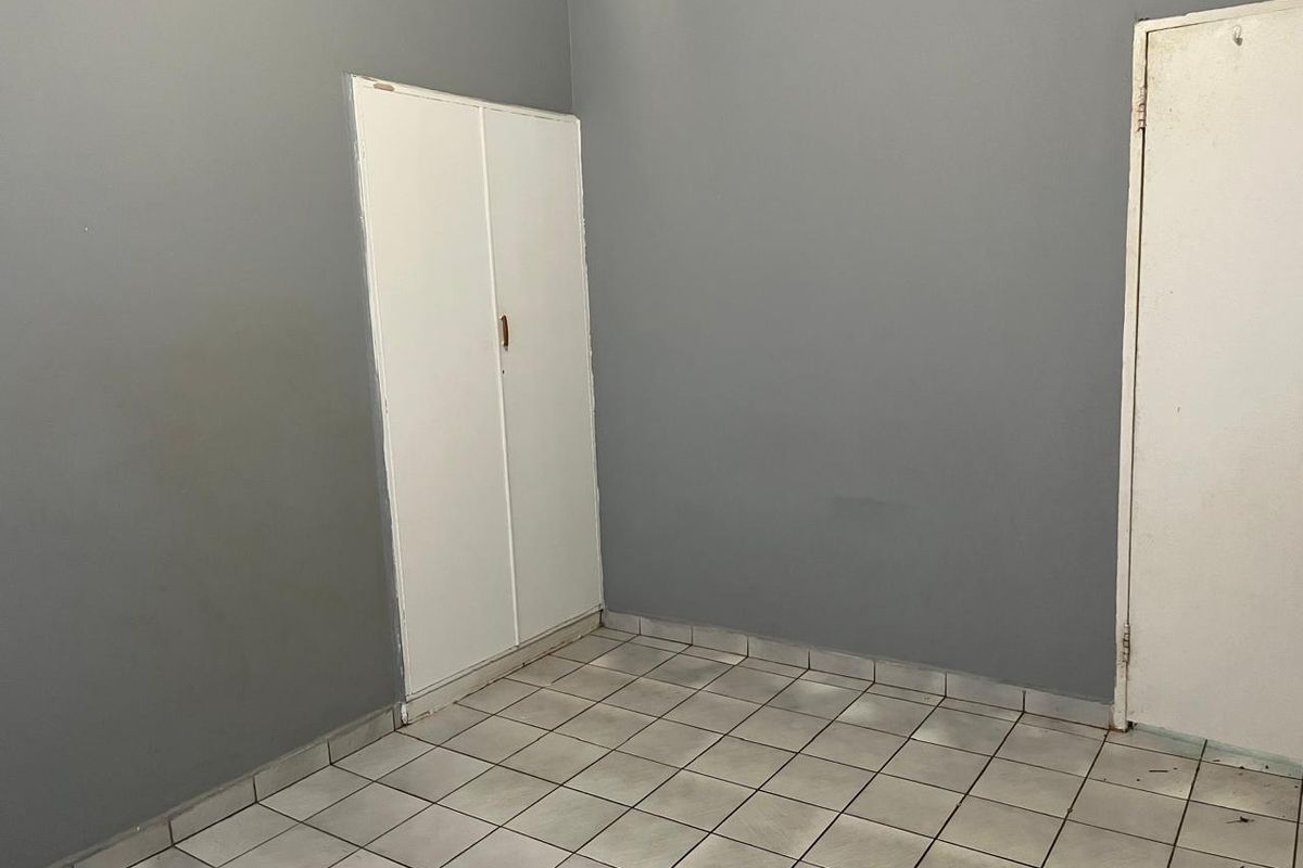 An empty bedroom featuring grey painted walls, white built-in cupboards, and tiled flooring, ready for personalization.