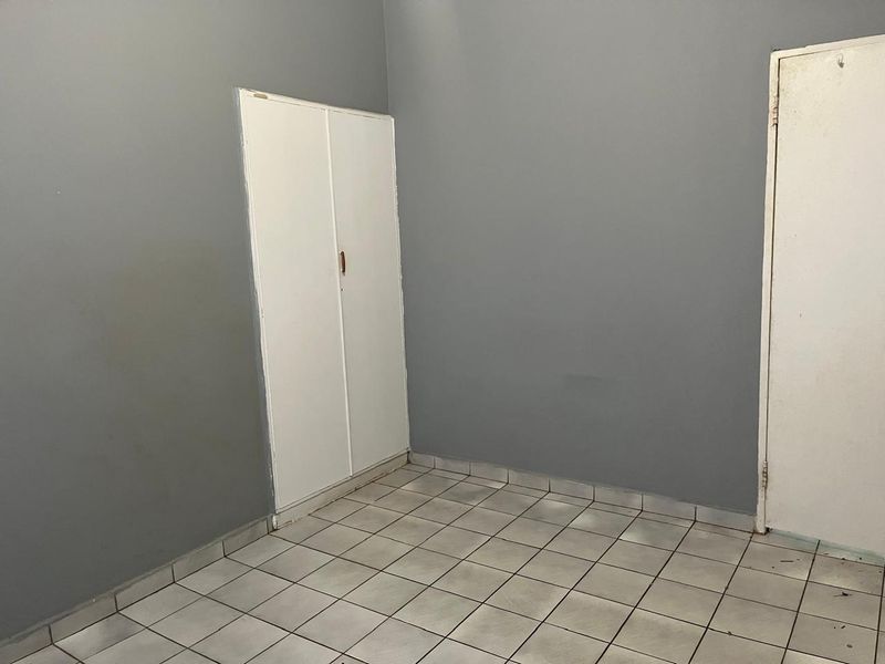 An empty bedroom featuring grey painted walls, white built-in cupboards, and tiled flooring, ready for personalization.