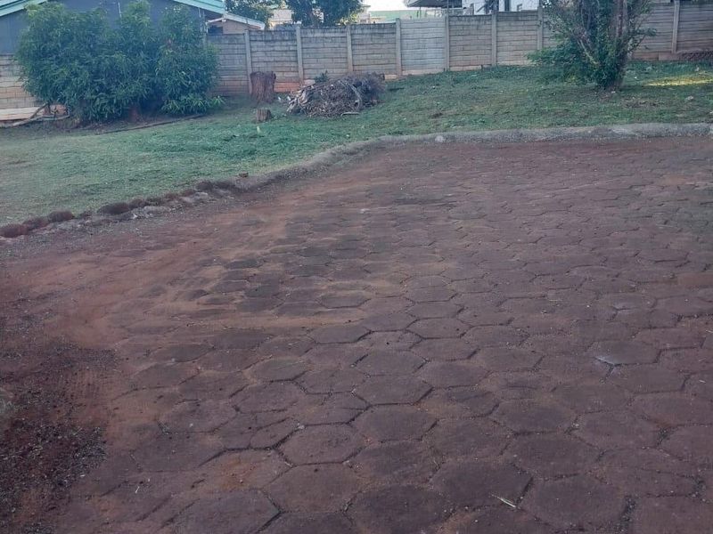 A rear outdoor area featuring a paved driveway, a precast concrete boundary wall, and a grassed garden space.