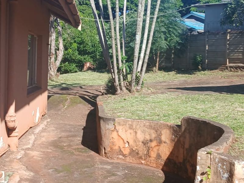 Rear exterior view of the property featuring a paved walkway, brick steps, and a weathered retaining wall set within a garden area.