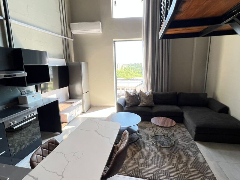 Modern open-plan apartment featuring a sleek kitchen with stone countertops, high ceilings, and a mezzanine level, offering a bright and contemporary living space.