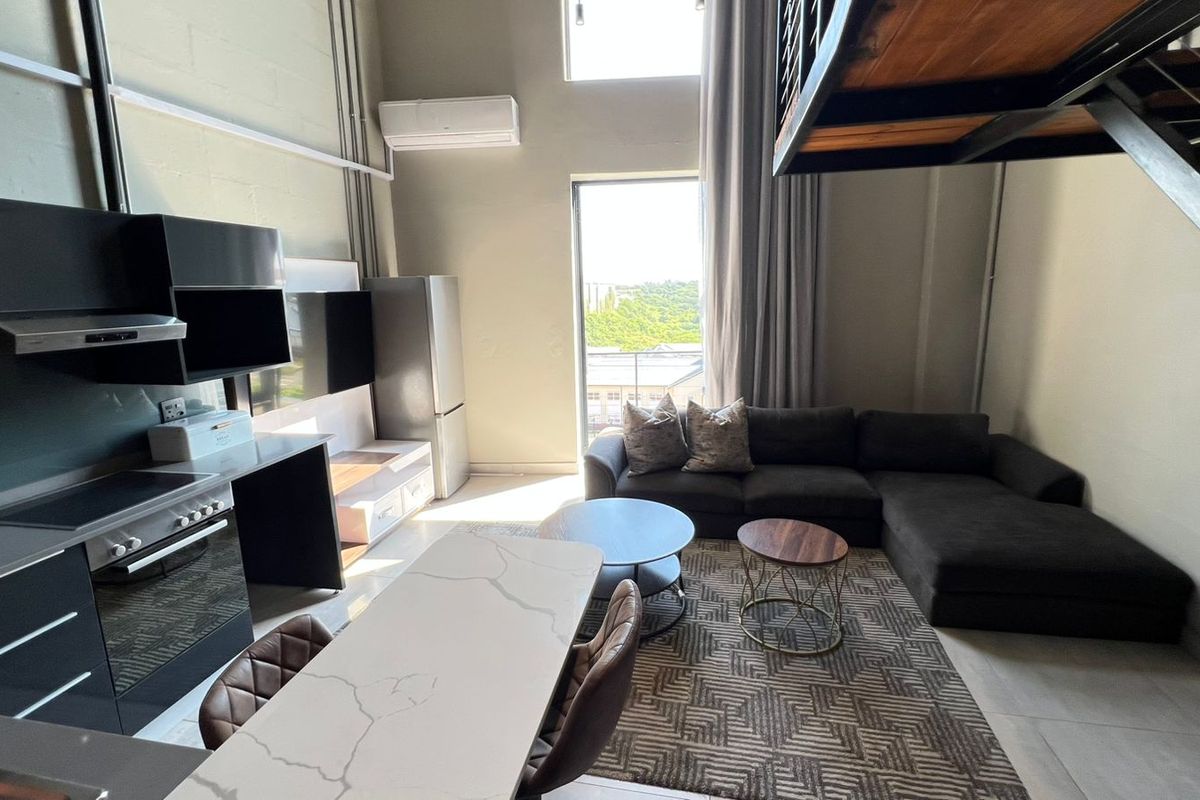 Modern open-plan apartment featuring a sleek kitchen with stone countertops, high ceilings, and a mezzanine level, offering a bright and contemporary living space.