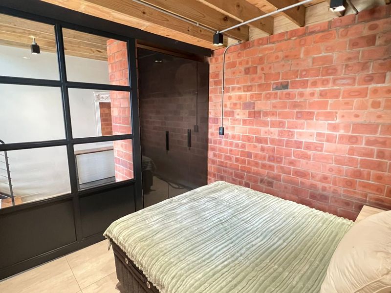 Modern bedroom featuring exposed brick walls, timber ceiling beams, and a stylish black steel-framed glass partition with integrated wardrobe storage.