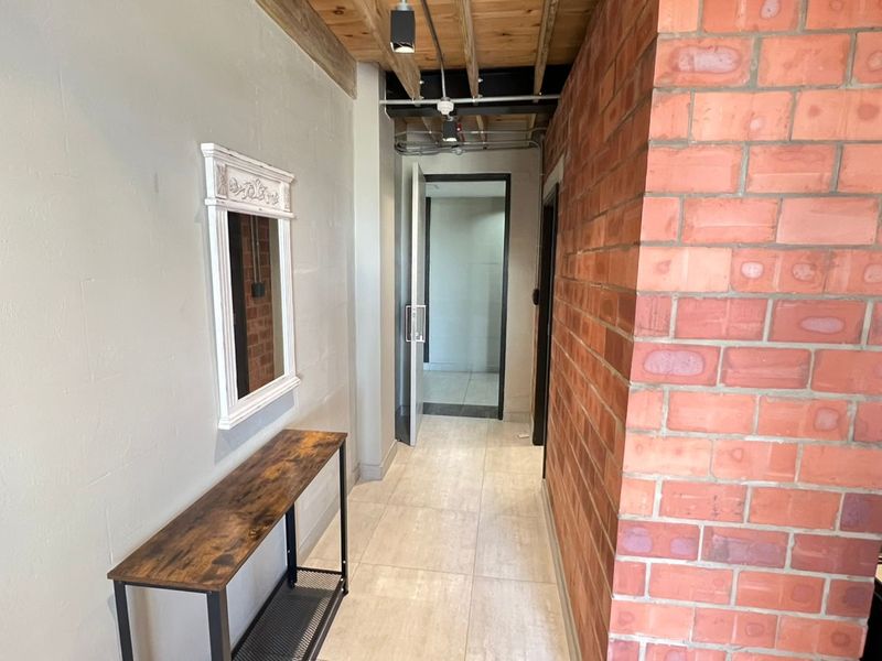 A modern hallway featuring exposed brick walls, a timber ceiling with exposed industrial-style conduit, and neutral tiled flooring.