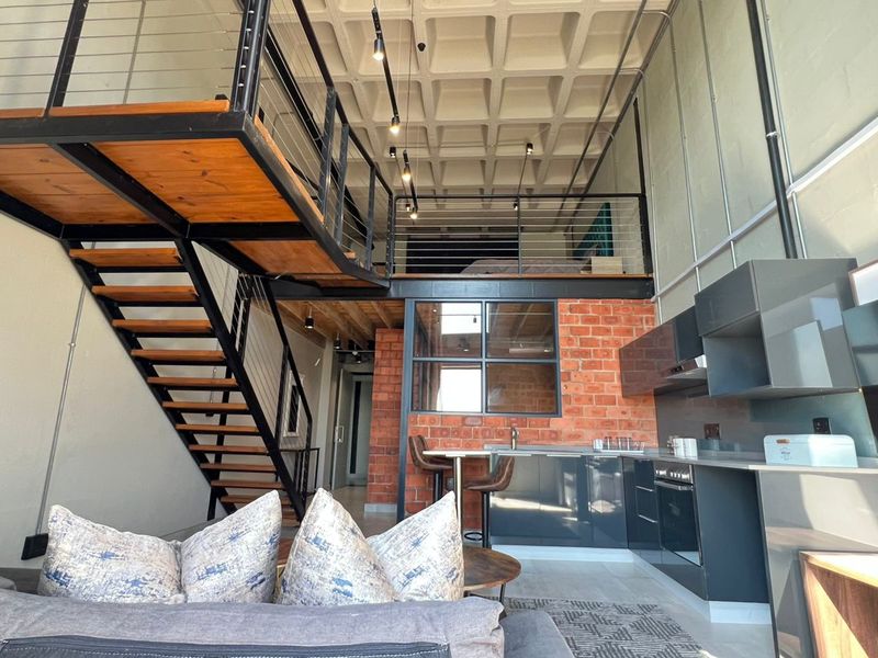Modern industrial-style open-plan apartment featuring a mezzanine level, exposed concrete waffle ceiling, brick feature wall, and a sleek contemporary kitchen.