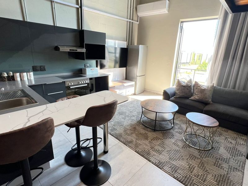 Modern open-plan apartment living area featuring a sleek kitchen with stone countertops, integrated appliances, and direct access to a balcony.