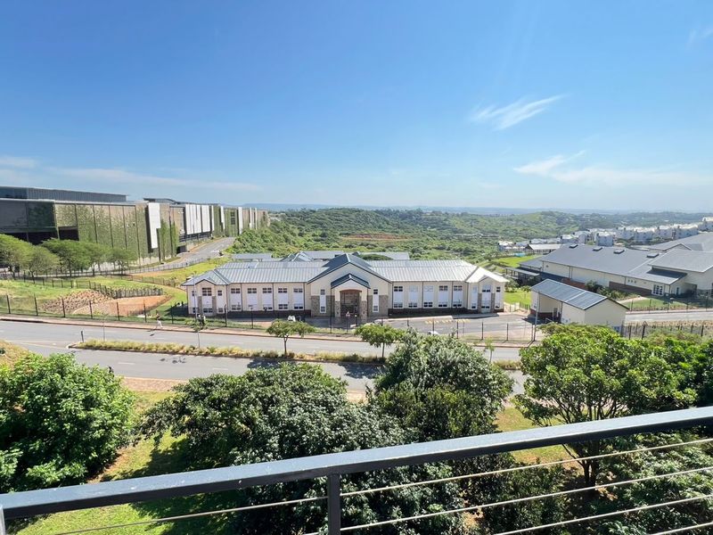 Elevated view from a balcony overlooking a suburban landscape with nearby commercial buildings and green spaces.
