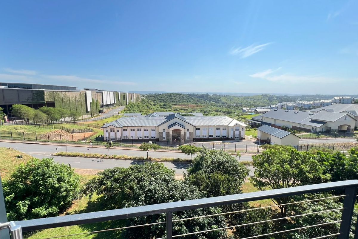 Elevated view from a balcony overlooking a suburban landscape with nearby commercial buildings and green spaces.