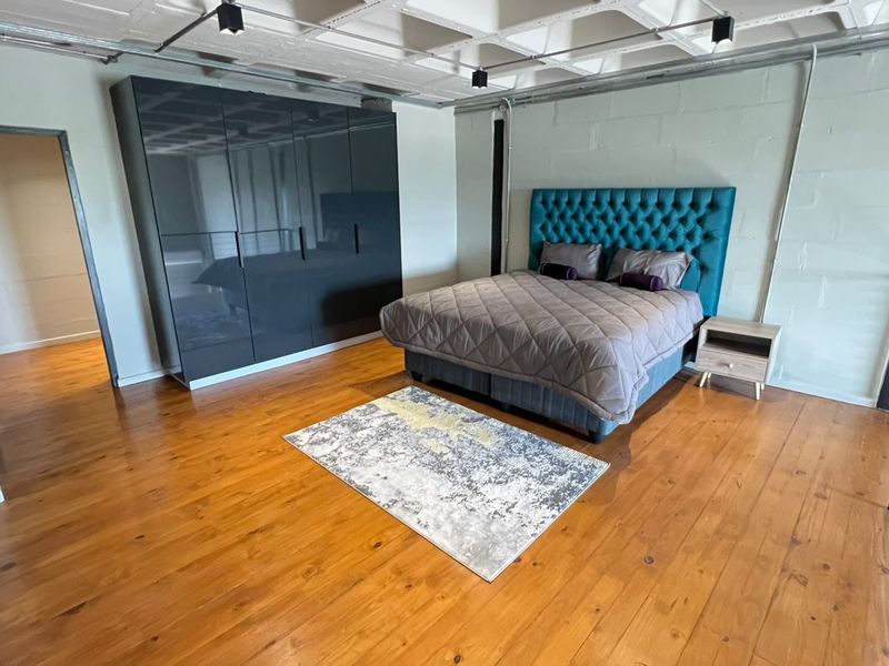 Spacious industrial-style bedroom featuring polished timber flooring, exposed ceiling structure, and a large built-in wardrobe with a sleek finish.