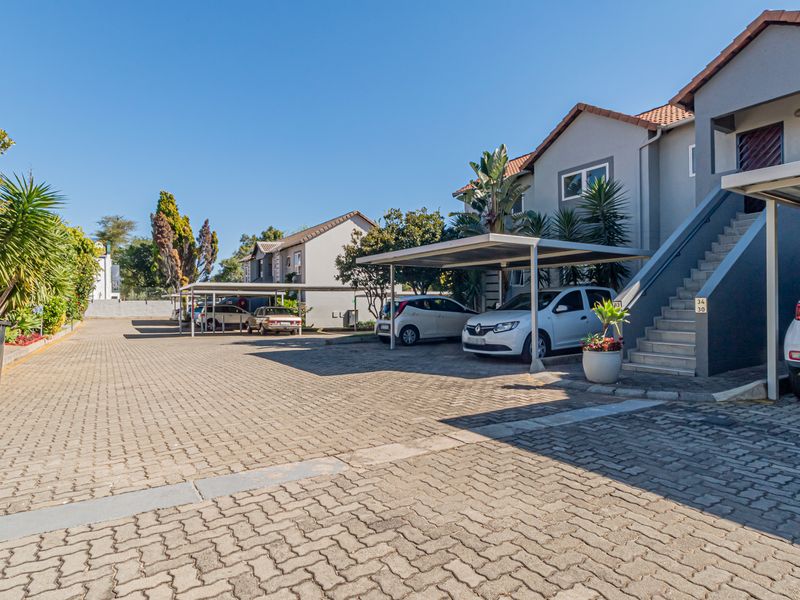 Exterior view of the apartment complex featuring a paved parking area with covered carports and external staircases leading to the units.