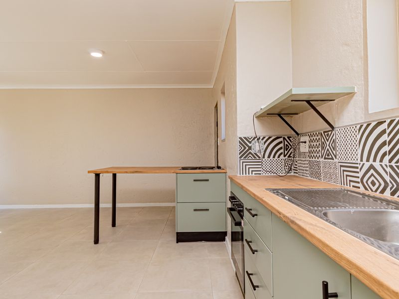 A clean, modern kitchen featuring light green cabinetry, wooden countertops, a patterned tile backsplash, and integrated cooking appliances in an open-plan layout.
