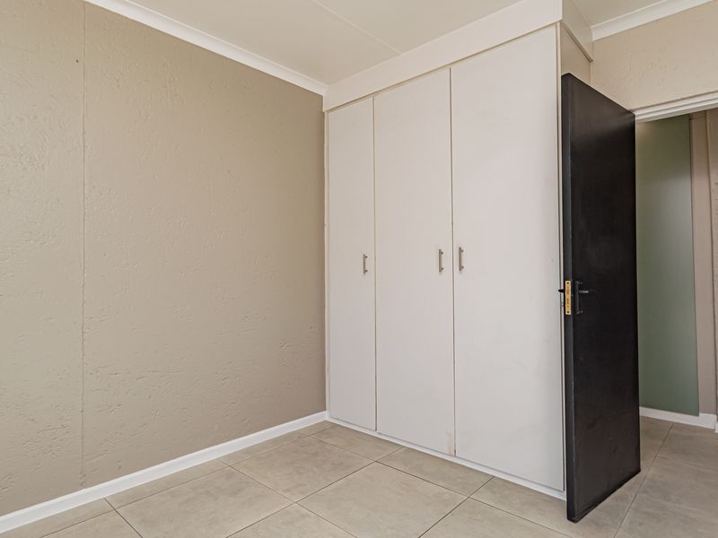A clean, empty bedroom featuring neutral wall tones, tiled flooring, and ample built-in cupboard storage space.