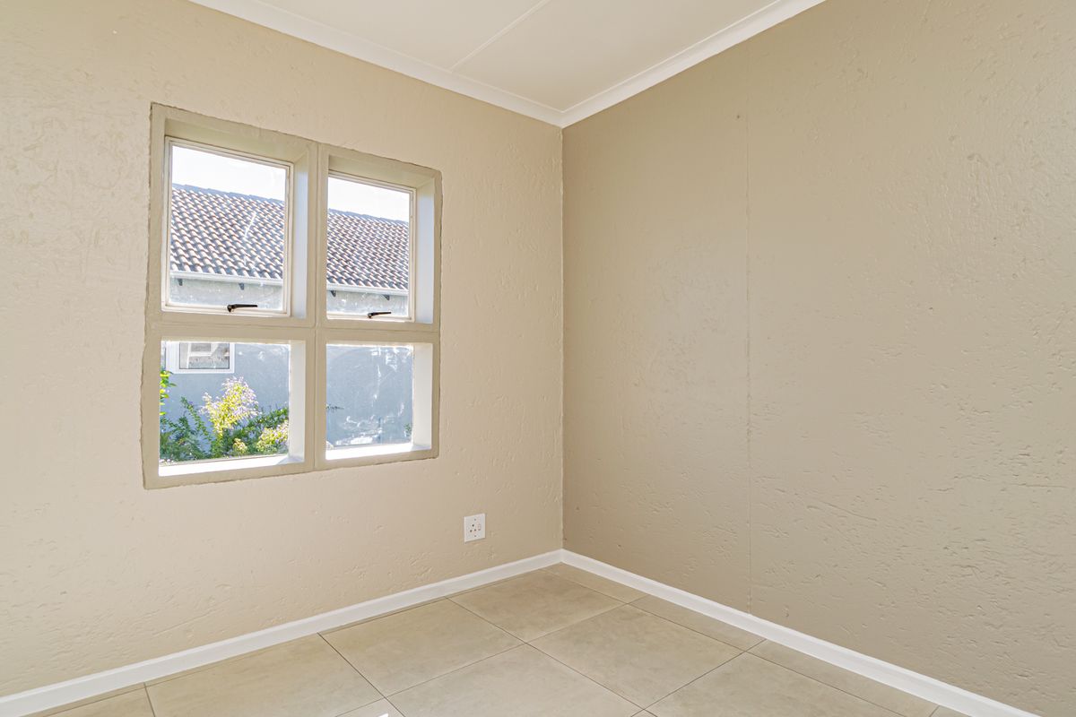 An empty bedroom featuring neutral textured walls, tiled flooring, and a casement window providing natural light.