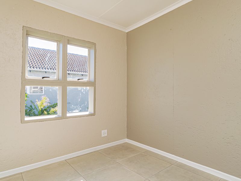 An empty bedroom featuring neutral textured walls, tiled flooring, and a casement window providing natural light.