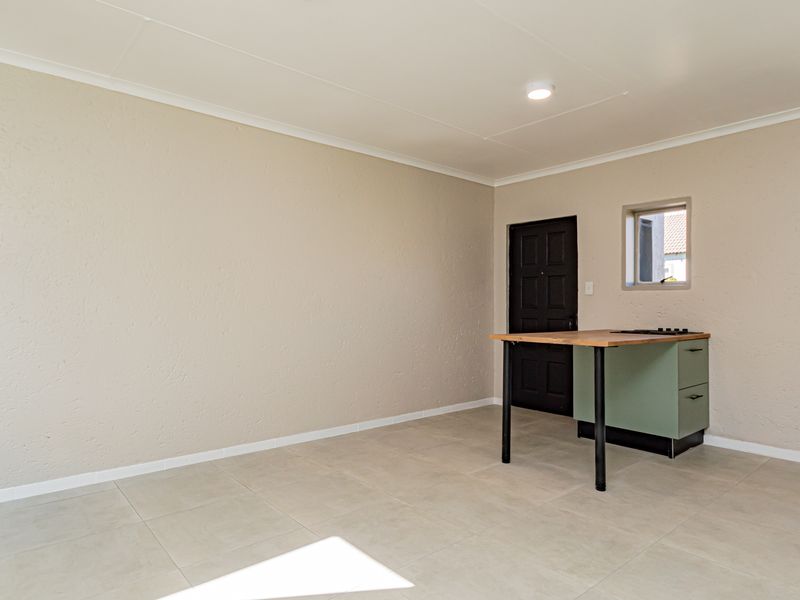An open-plan living and kitchen area featuring neutral walls, tiled flooring, and a compact kitchen unit with a built-in oven and cooktop.