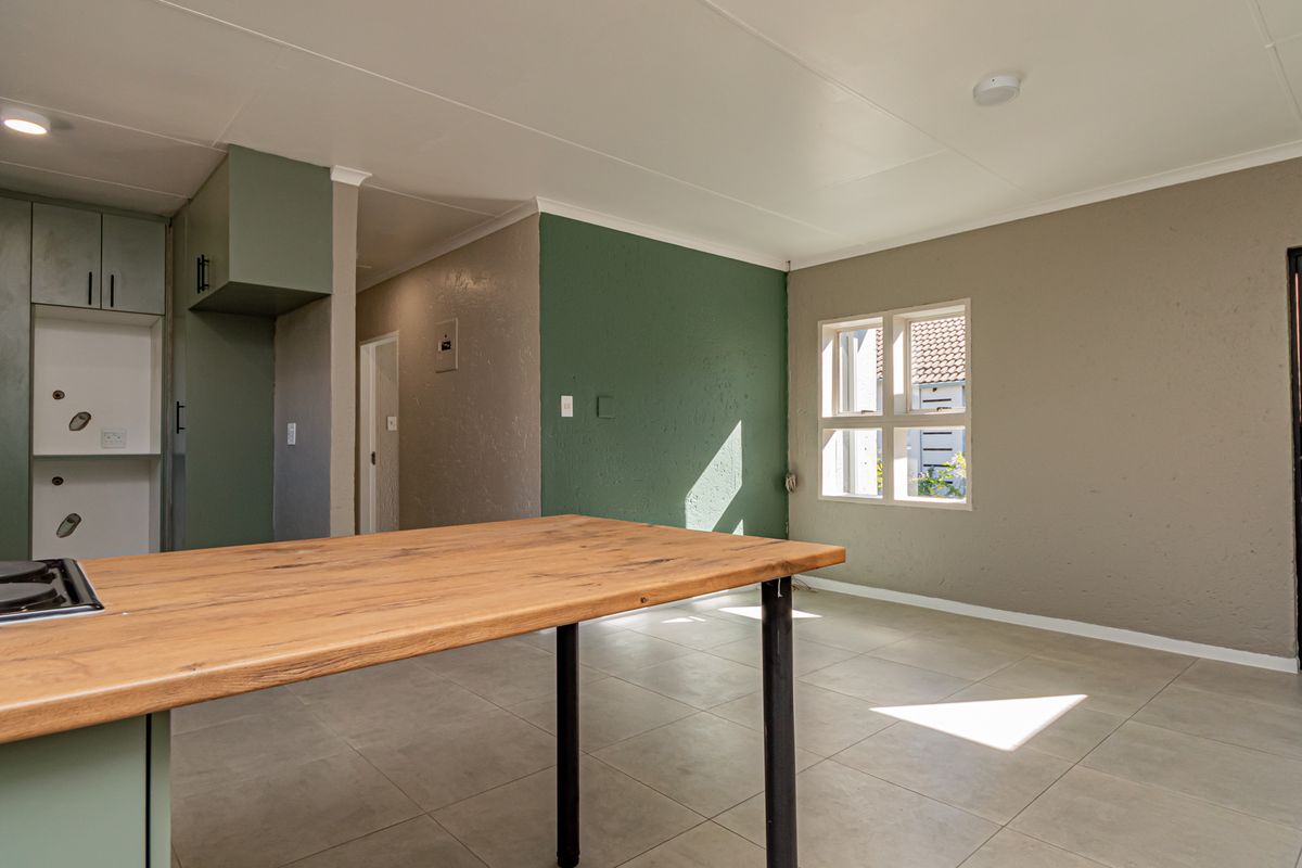 An open-plan living and kitchen area featuring tiled floors, built-in cabinetry with a hob, and direct access to the exterior.