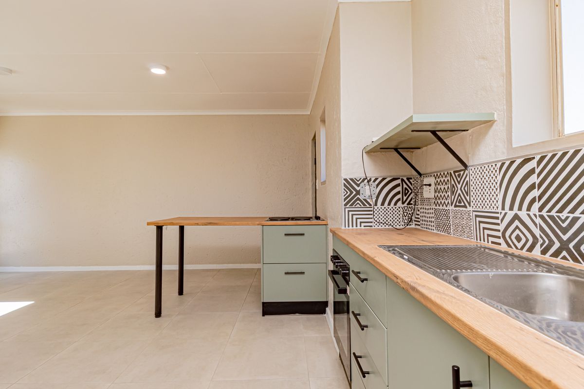 A clean, modern kitchen featuring light green cabinetry, wooden countertops, a patterned tile backsplash, and integrated cooking appliances in an open-plan layout.